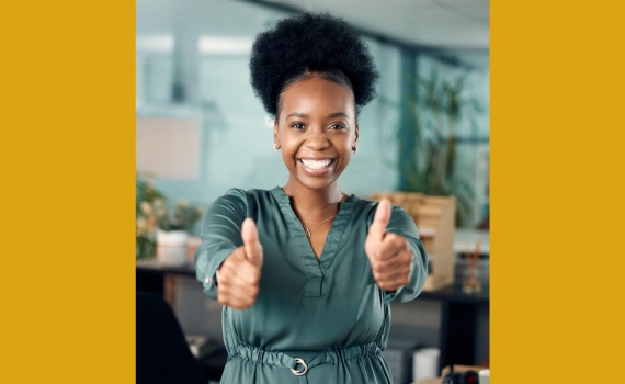 Young black business woman in office setting with two thumbs Up. Pathways to Business Success Through Grant Writing_NCBW News Feed Post_Featured Image_570 x 350
